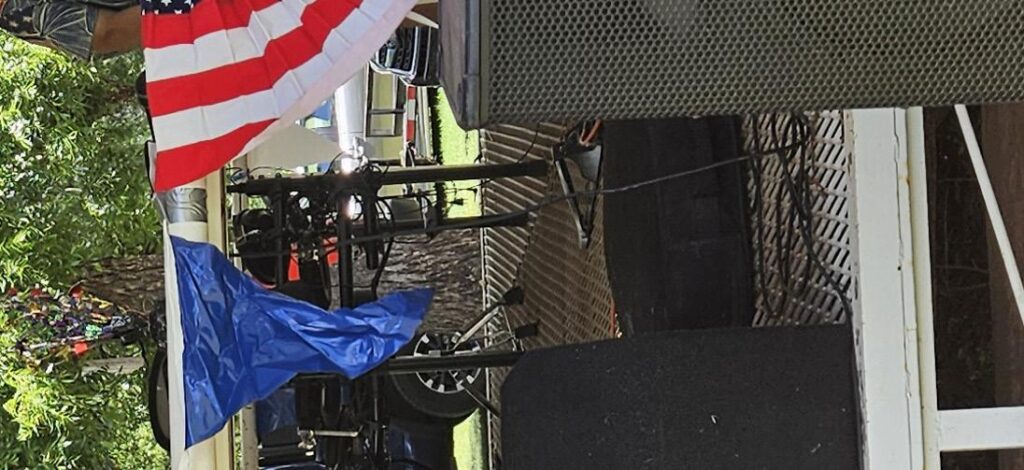 Close-up view of a patriotic stage setup featuring an American flag and Oklahoma flag, with sound and lighting equipment prepared for live entertainment.